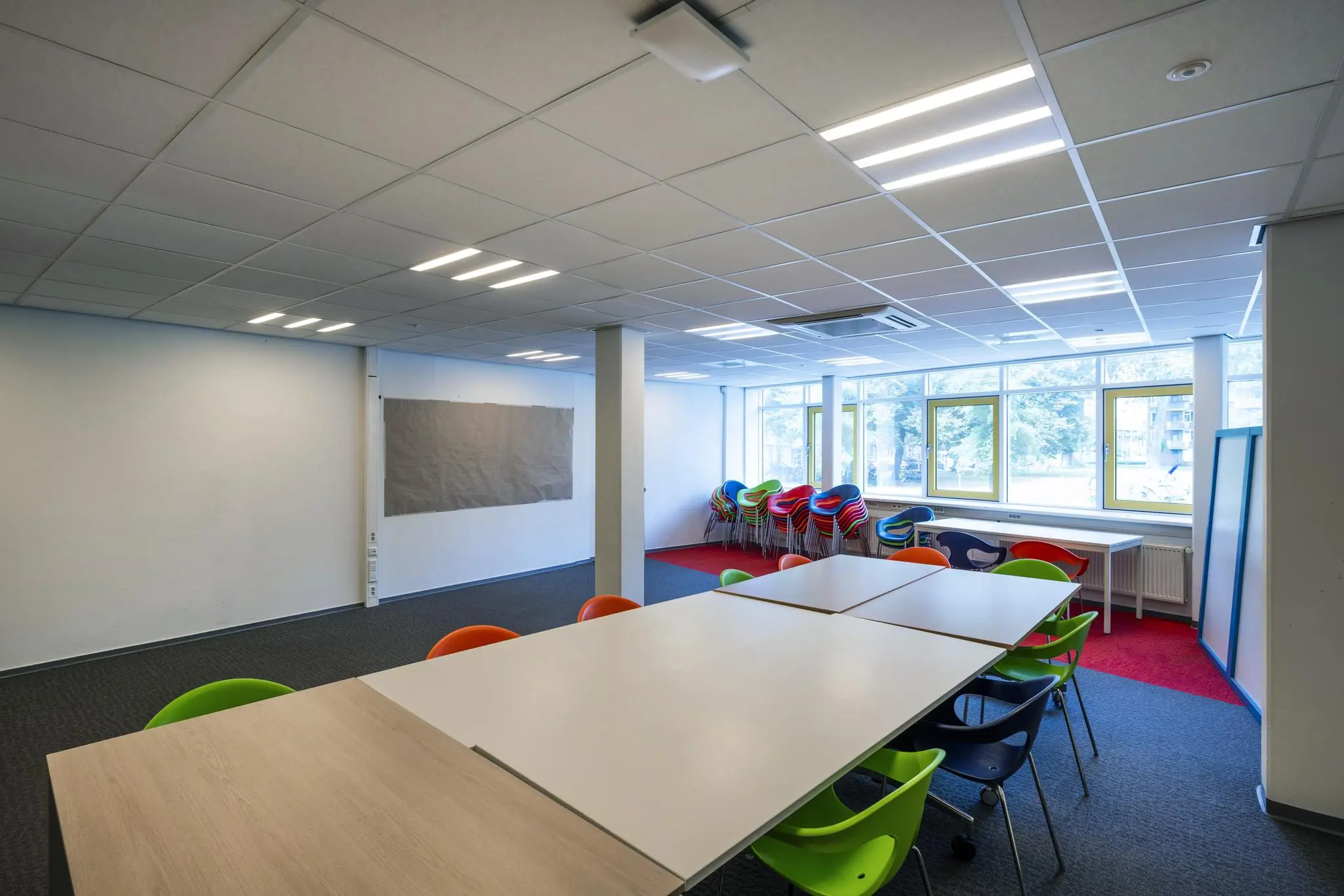 Licht en kleurrijk lokaal aan de Jan Tooropstraat met stapels stoelen en tafels in een open opstelling.